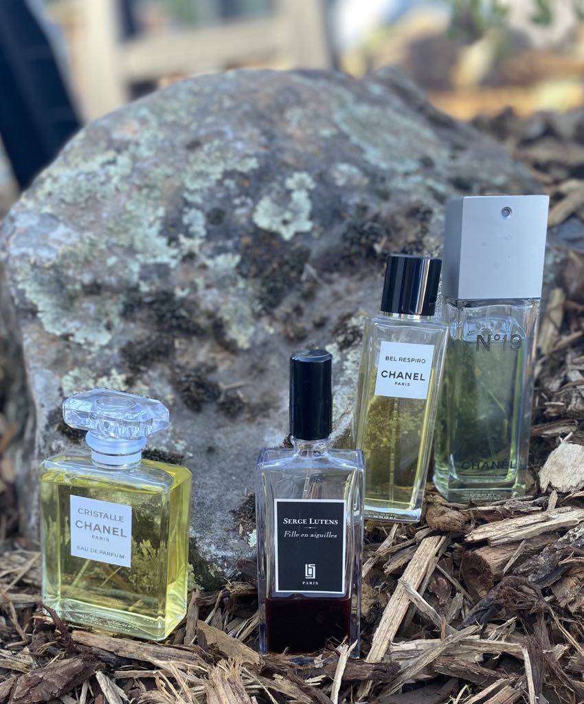 4 perfume bottles sitting next to a rock on top of wood chips