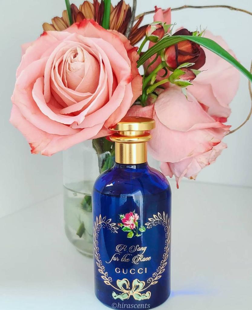 A bottle of perfume in front of a vase of roses and other flowers.