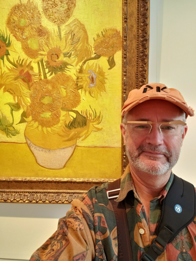 Paul standing next to a Van Gogh painting of sunflowers